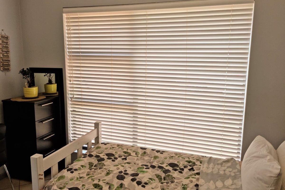 A bedroom featuring tiled flooring and large window fitted with white venetian blinds.