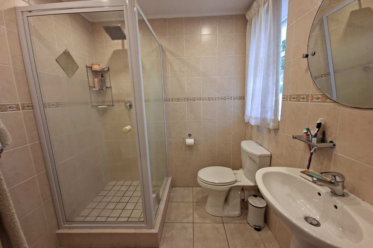 A functional bathroom featuring a glass-enclosed shower, pedestal basin, and toilet, finished with neutral wall and floor tiling.
