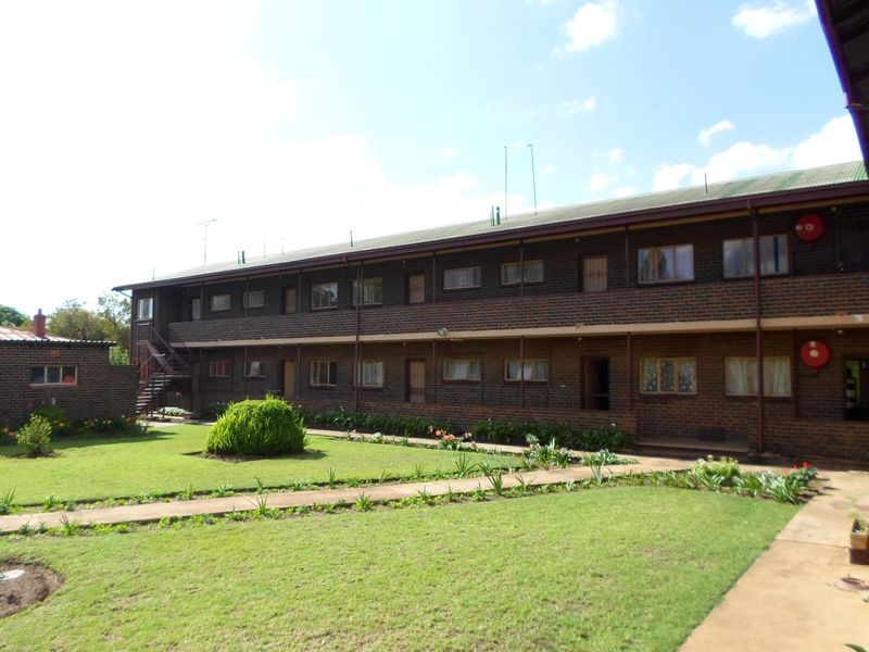 A multi-story apartment building exterior featuring a brick facade, metal roofing, and a shared garden area with concrete pathways.