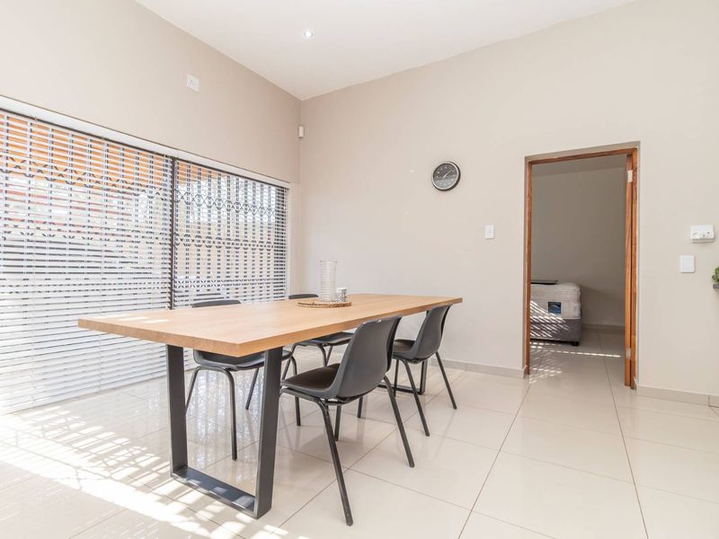A bright dining area featuring large sliding glass doors with security gates, neutral tiled flooring, and recessed downlighting.