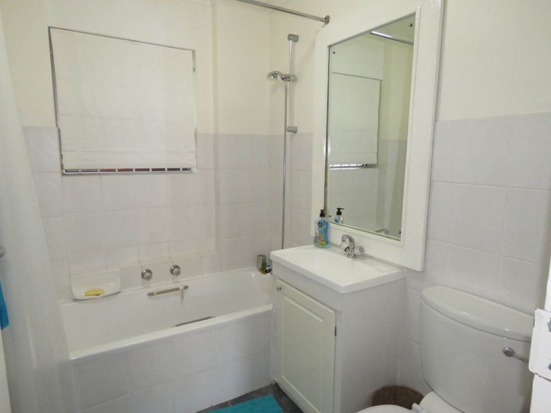 A functional bathroom featuring a bathtub with shower attachment, a vanity unit with integrated basin, and a wall-mounted mirror.
