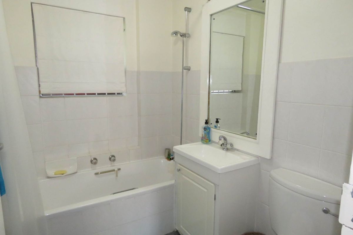 A functional bathroom featuring a bathtub with shower attachment, a vanity unit with integrated basin, and a wall-mounted mirror.
