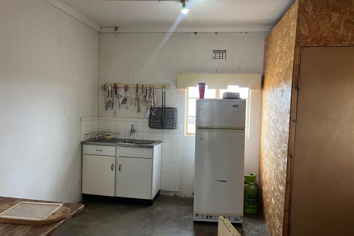 A basic utility kitchen area featuring a small sink unit, concrete flooring, and an unfinished partition wall.