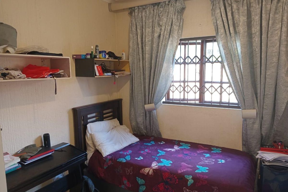 A compact bedroom featuring a window with a security gate and wall-mounted shelving units.