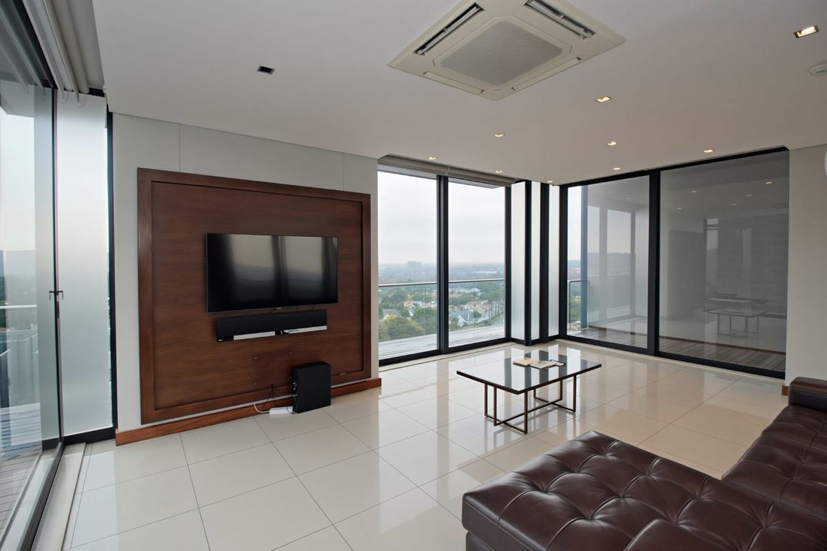 Modern penthouse living area featuring large floor-to-ceiling windows, polished tile flooring, recessed ceiling lighting, and a built-in wooden media wall.