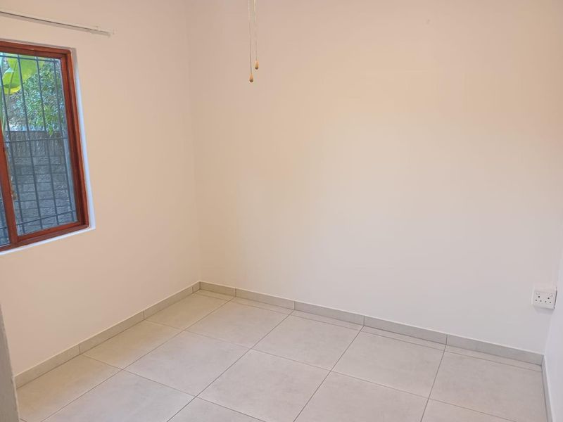 A clean, empty bedroom featuring neutral tiled flooring, a wooden-framed window with security bars, and a simple ceiling pull switch.