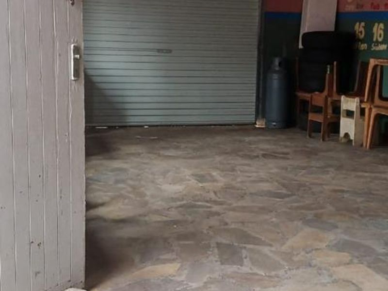 A spacious garage featuring a roller shutter door, exposed timber rafters, and durable stone flooring, offering ample storage or parking space.
