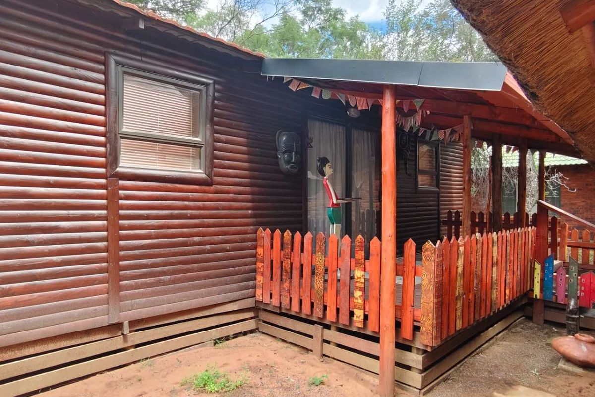A rustic log cabin exterior featuring a covered wooden deck, timber wall construction, and a decorative picket fence.