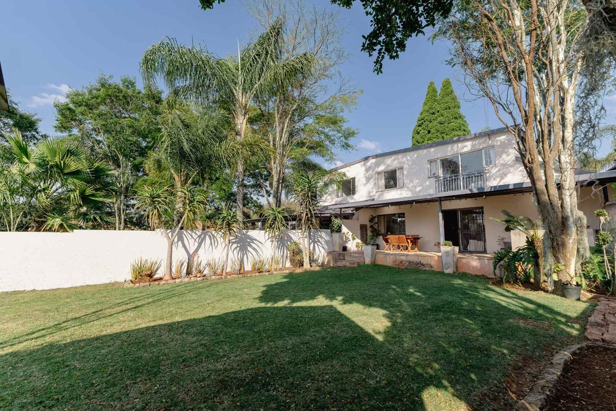 Rear view of the two-story house featuring a spacious lawn, landscaped garden, boundary wall, and an upper-level balcony with sliding door access.