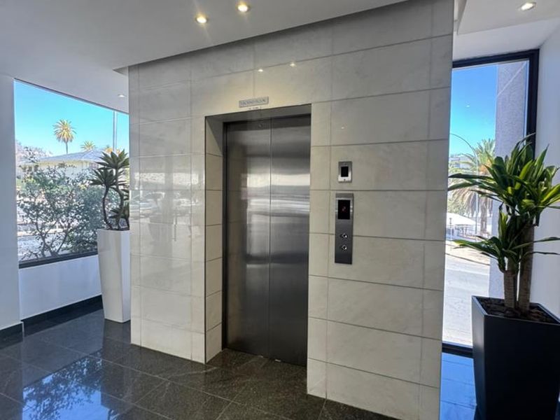 Modern office building lobby featuring a stainless steel elevator, polished granite flooring, and elegant marble wall cladding with natural light.