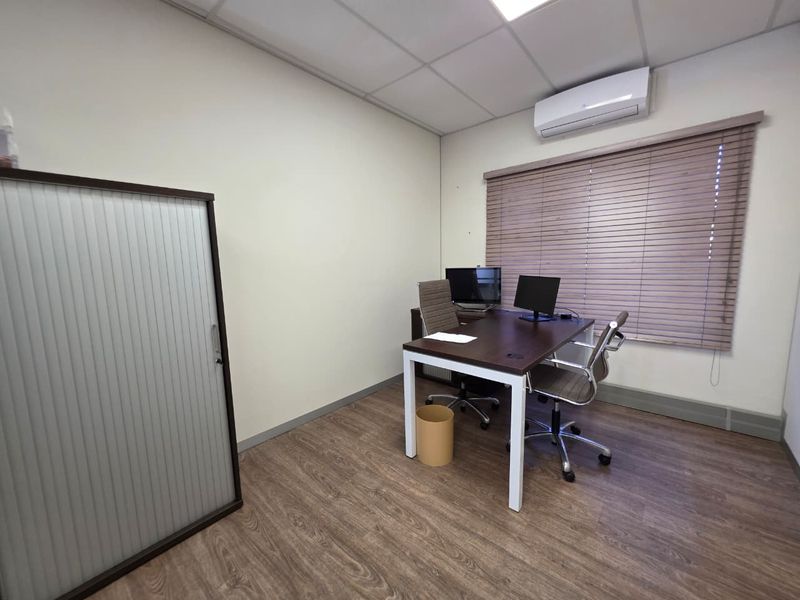 A functional office space featuring laminate wood flooring, a suspended ceiling, integrated air conditioning, and fitted timber blinds.
