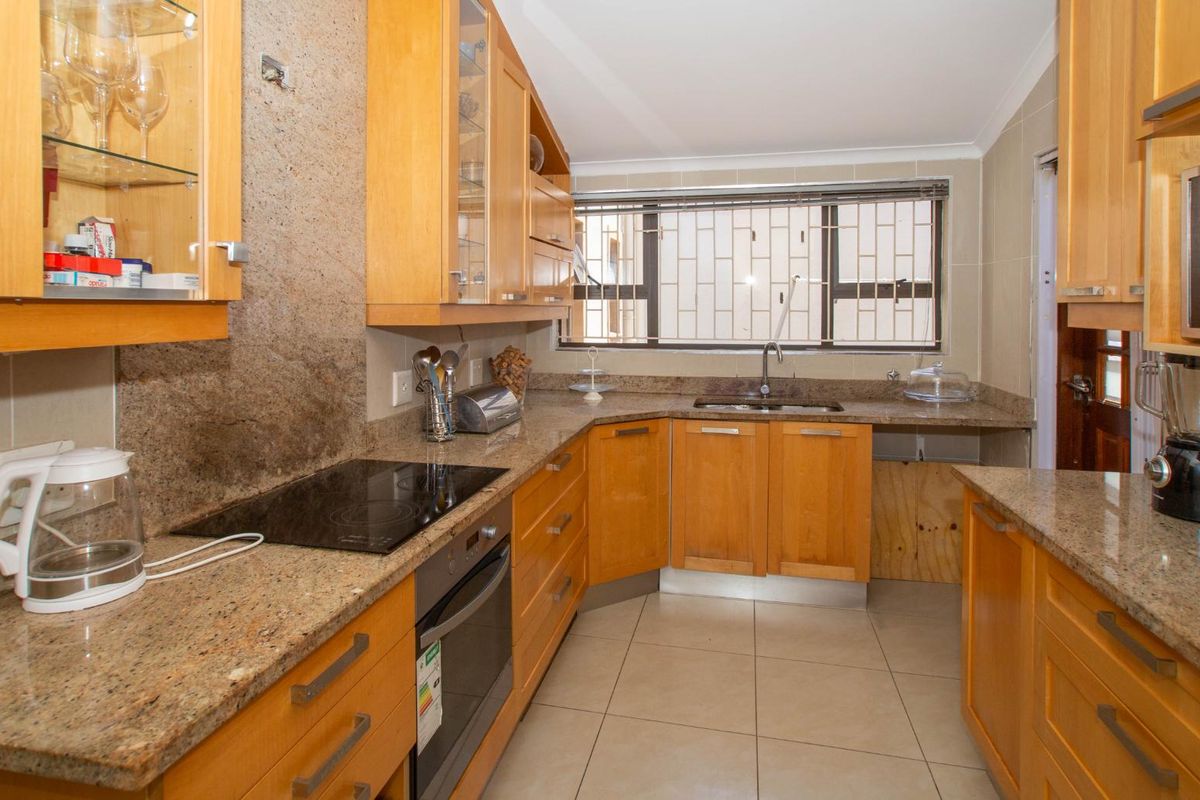 A functional kitchen featuring light wood cabinetry, granite countertops, a built-in oven, electric hob, and tiled flooring with a window overlooking the exterior.