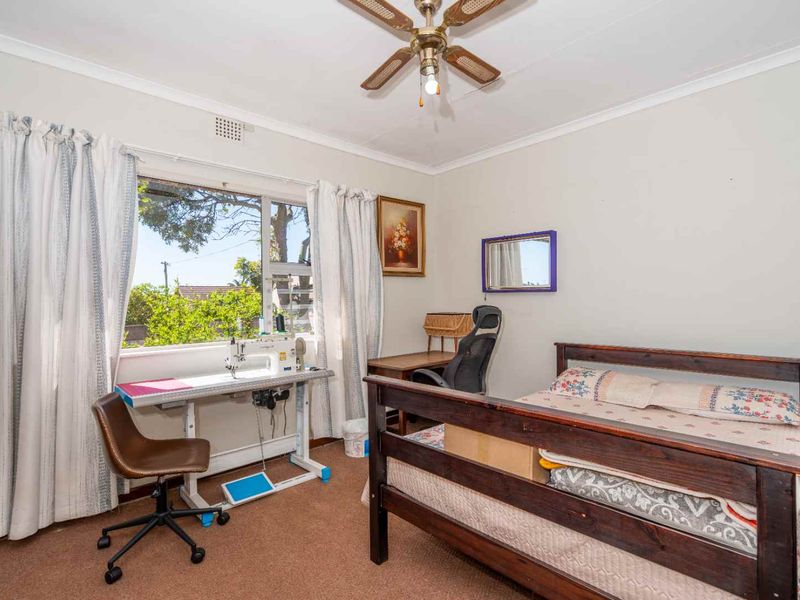 A functional bedroom featuring carpet flooring, a ceiling fan, and large windows providing natural light.