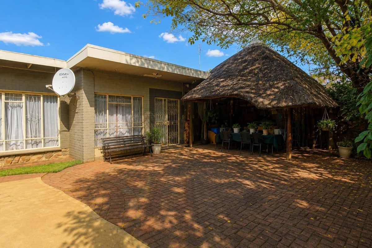 A rear exterior view featuring a paved patio area and a traditional thatched lapa, providing a shaded outdoor entertainment space.