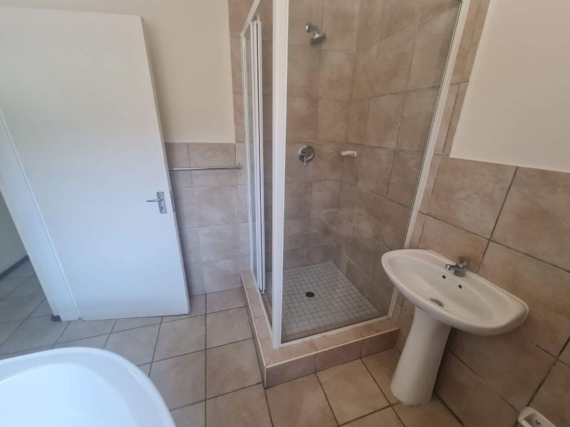 A functional bathroom featuring a corner shower enclosure, pedestal basin, and neutral floor and wall tiling.