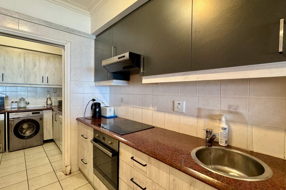 A functional kitchen featuring dark upper cabinetry, stone countertops, integrated appliances, and a tiled backsplash, with an adjacent laundry area visible.