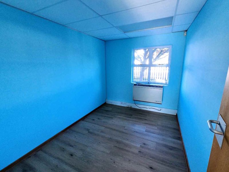 A vacant office space featuring bright blue walls, wood-look laminate flooring, a suspended ceiling, and a wall-mounted HVAC unit.