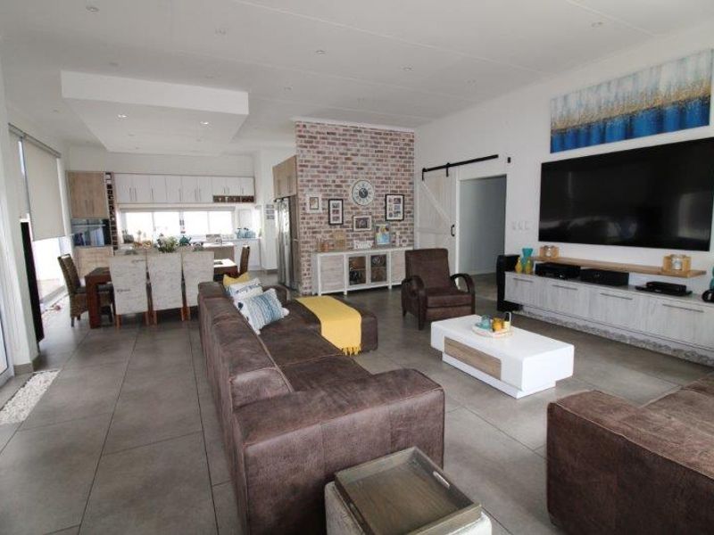 Spacious open-plan living and dining area featuring a striking exposed brick wall, modern tiled flooring, and seamless flow into the integrated kitchen space.