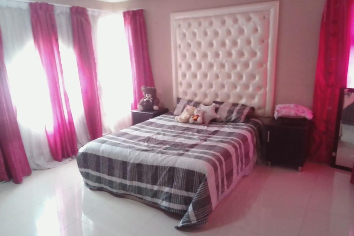 A bedroom featuring tiled flooring and a large tufted headboard, illuminated by natural light through window curtains.