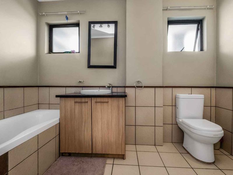 A functional bathroom featuring a vanity with a vessel sink, a bathtub, and a toilet, finished with neutral wall and floor tiling.