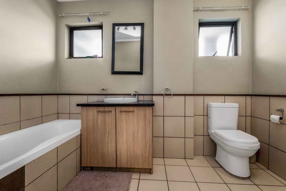 A functional bathroom featuring a vanity with a vessel sink, a bathtub, and a toilet, finished with neutral wall and floor tiling.