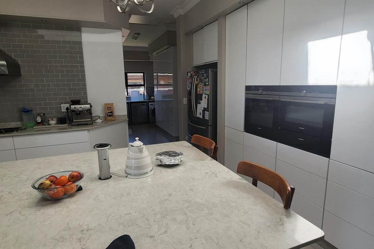 Modern kitchen featuring a large central island with stone countertop, integrated double ovens, sleek cabinetry, and a subway tile backsplash.