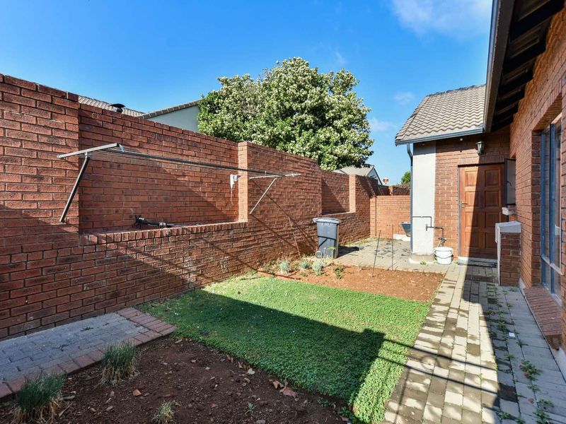 A private rear courtyard featuring a brick boundary wall, paved walkway, and a small garden area with a wall-mounted clothesline.