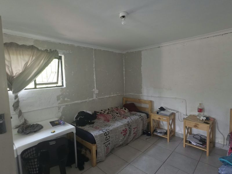 A bedroom featuring tiled flooring and exposed electrical conduit, currently requiring wall finishing and painting to improve the overall aesthetic and condition.