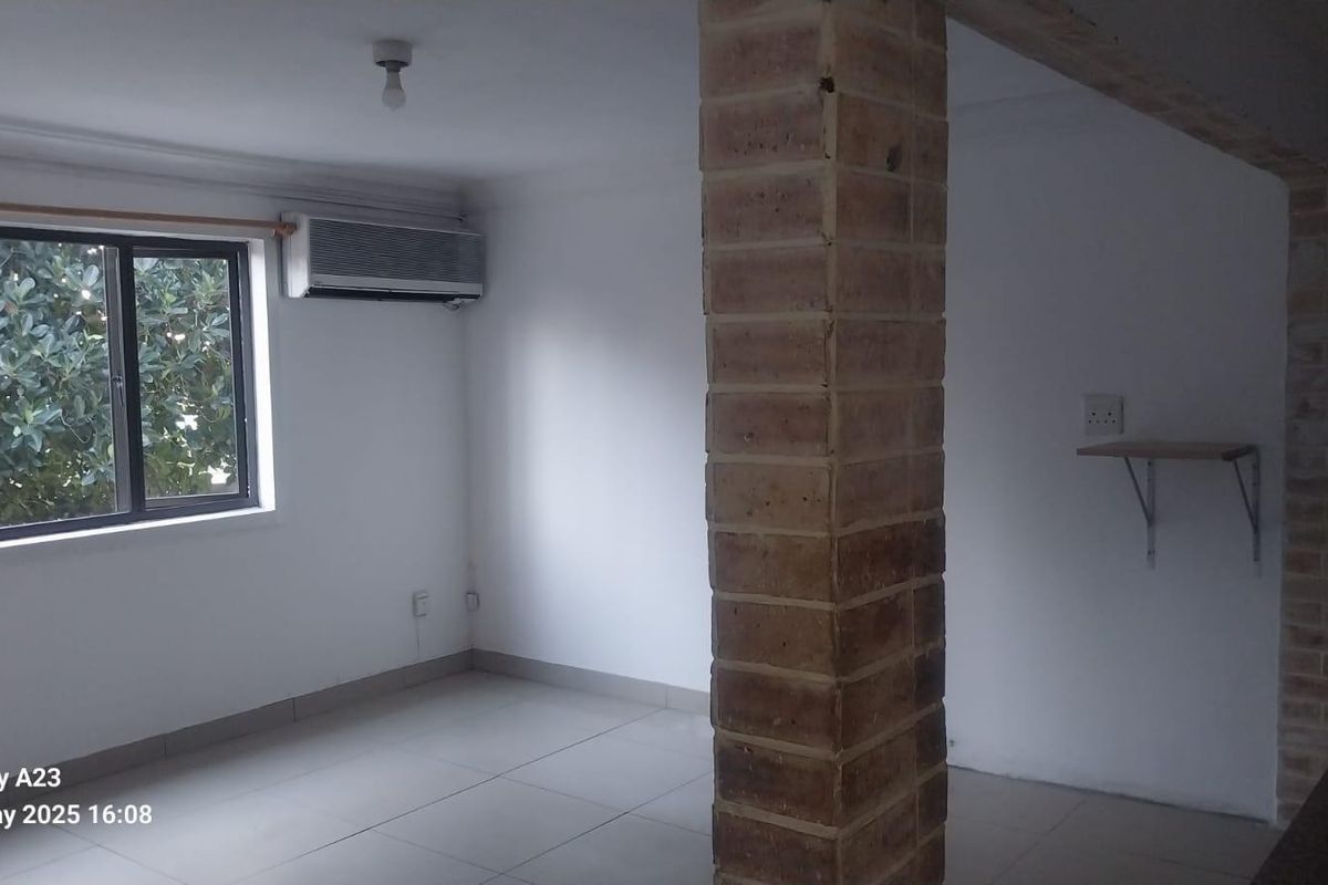 An empty living area featuring tiled floors, an air conditioning unit, and a prominent exposed brick pillar, offering a blank canvas for interior design.