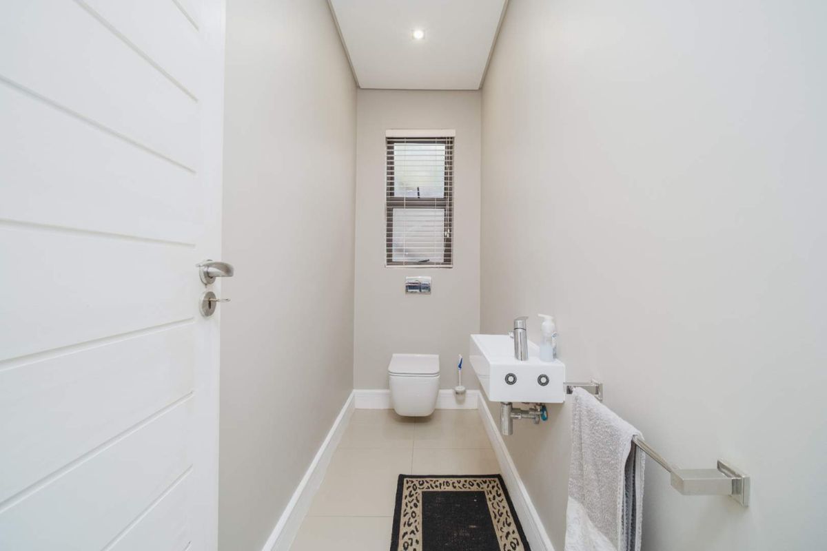 A modern guest bathroom featuring a wall-mounted toilet, a sleek floating basin, and neutral floor tiling.