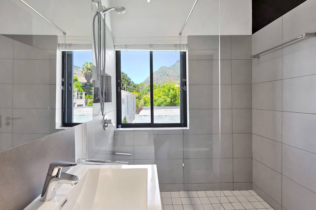 Modern bathroom featuring a walk-in shower with glass screen, contemporary basin with chrome mixer, and large wall mirror, offering a clean and bright aesthetic.
