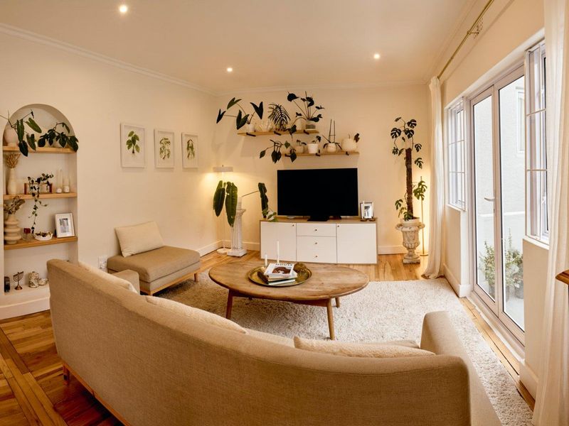 A bright and inviting living room featuring hardwood floors, recessed lighting, crown molding, and an arched built-in display niche with access to a patio.