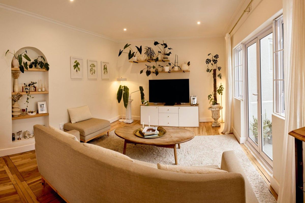 A bright and inviting living room featuring hardwood floors, recessed lighting, crown molding, and an arched built-in display niche with access to a patio.