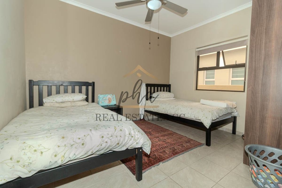A functional bedroom featuring tiled flooring, a ceiling fan, and a built-in wardrobe, providing practical storage and comfortable living space.