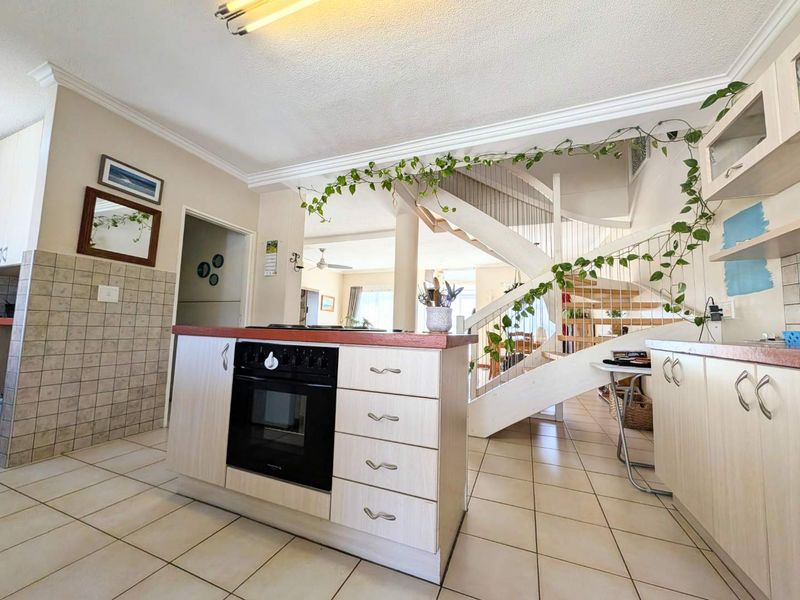 Open plan kitchen area featuring built-in oven and hob, tiled flooring, and a central staircase leading to the upper level.