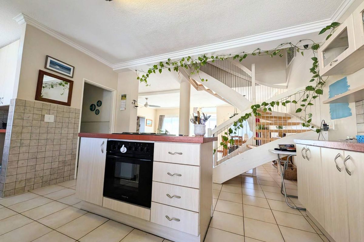 Open plan kitchen area featuring built-in oven and hob, tiled flooring, and a central staircase leading to the upper level.