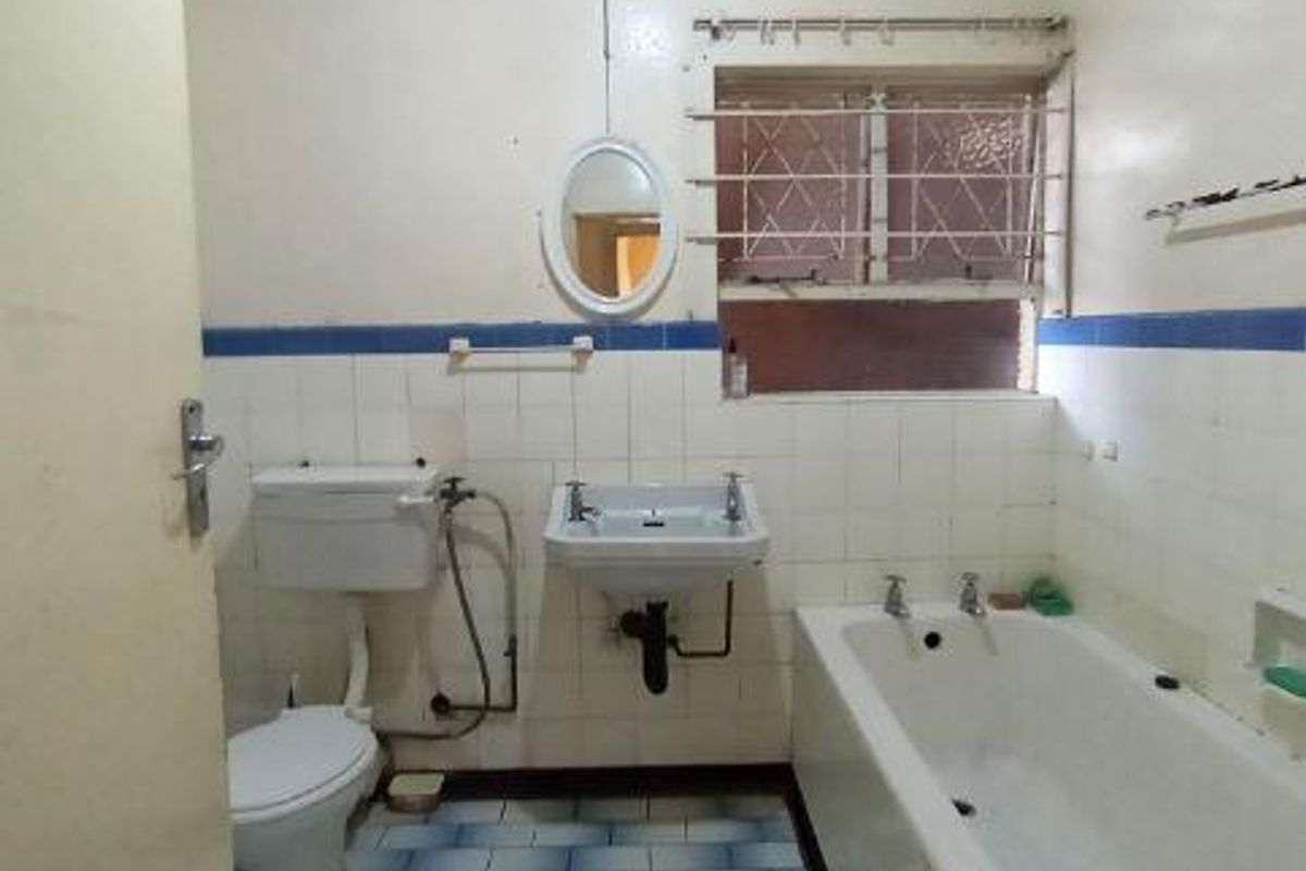 A dated bathroom featuring a standard bathtub, pedestal washbasin, and flush toilet, requiring cosmetic updates and tile repairs to modernize the space.