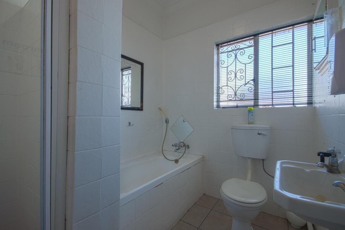 A functional bathroom featuring a built-in bathtub, a standard toilet, a wall-mounted basin, and a shower enclosure with white tiled walls.