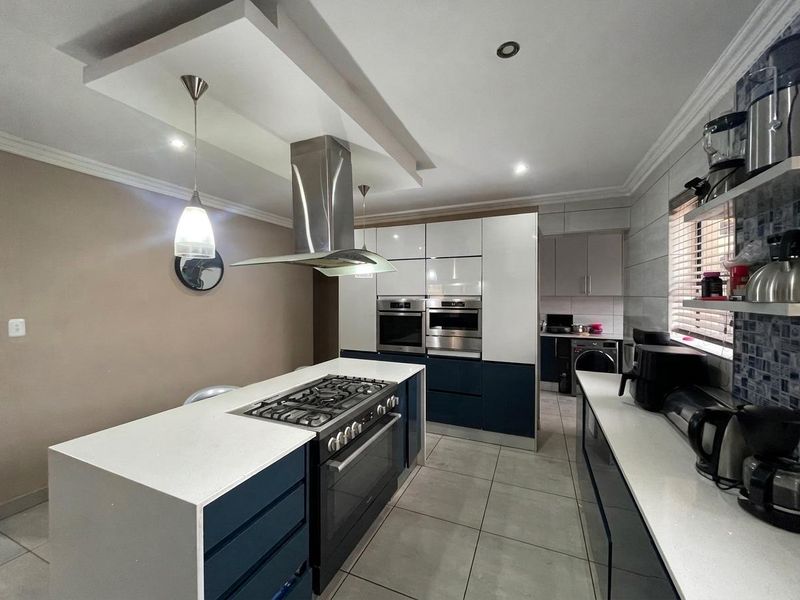 Modern kitchen featuring a central island with a gas cooktop, built-in ovens, sleek cabinetry, stone countertops, and a stylish drop ceiling with integrated lighting.