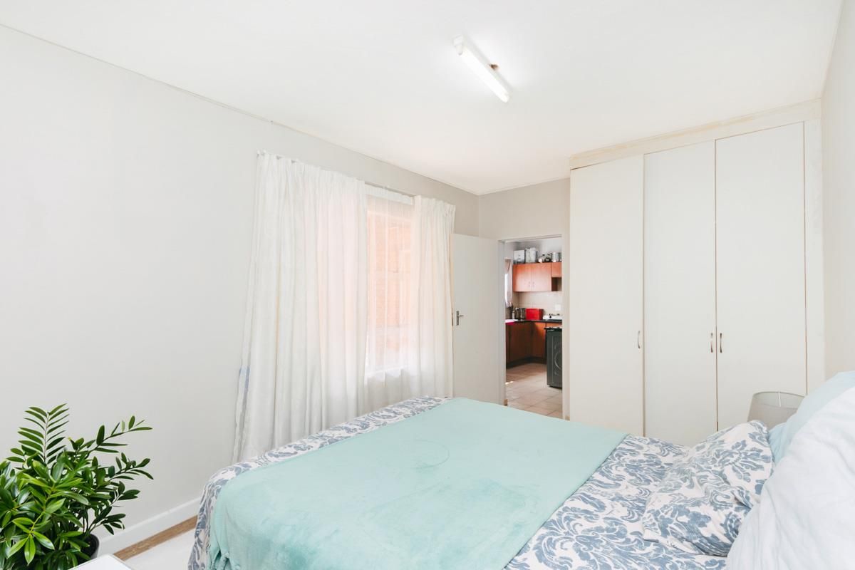 A bedroom featuring built-in cupboards and a view through to the kitchen area.