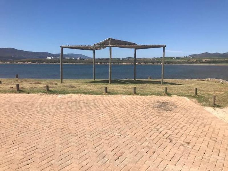 A scenic view of the waterfront featuring a paved driveway area, timber pergola structure, and surrounding landscape.