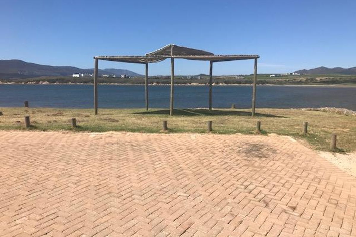 A scenic view of the waterfront featuring a paved driveway area, timber pergola structure, and surrounding landscape.