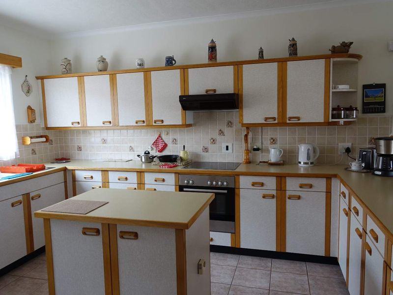 A functional kitchen featuring traditional wood-trimmed cabinetry, laminate countertops, a central island, and integrated appliances with a tiled backsplash and flooring.