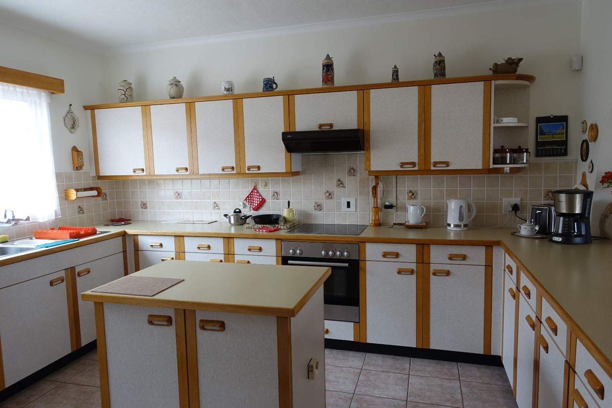A functional kitchen featuring traditional wood-trimmed cabinetry, laminate countertops, a central island, and integrated appliances with a tiled backsplash and flooring.