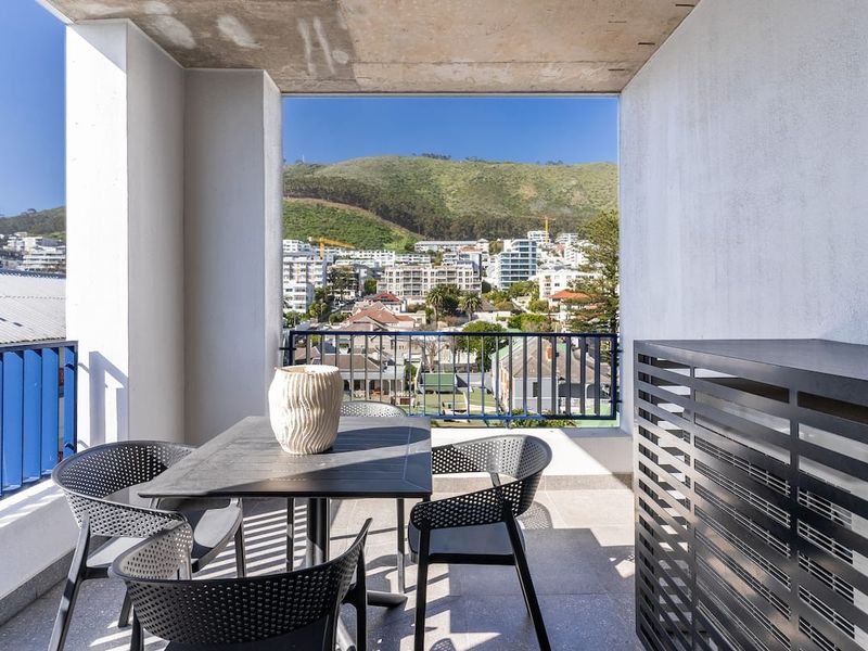 A modern covered balcony featuring tiled flooring, a metal balustrade, and an integrated air conditioning unit enclosure, offering scenic mountain and urban views.