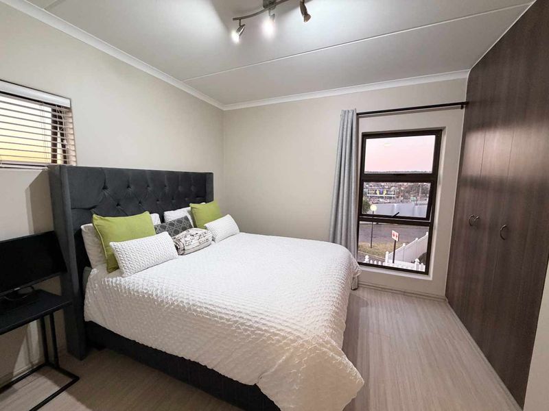 A well-maintained bedroom featuring laminate flooring, built-in cupboards, and modern track lighting, offering a clean and functional living space.