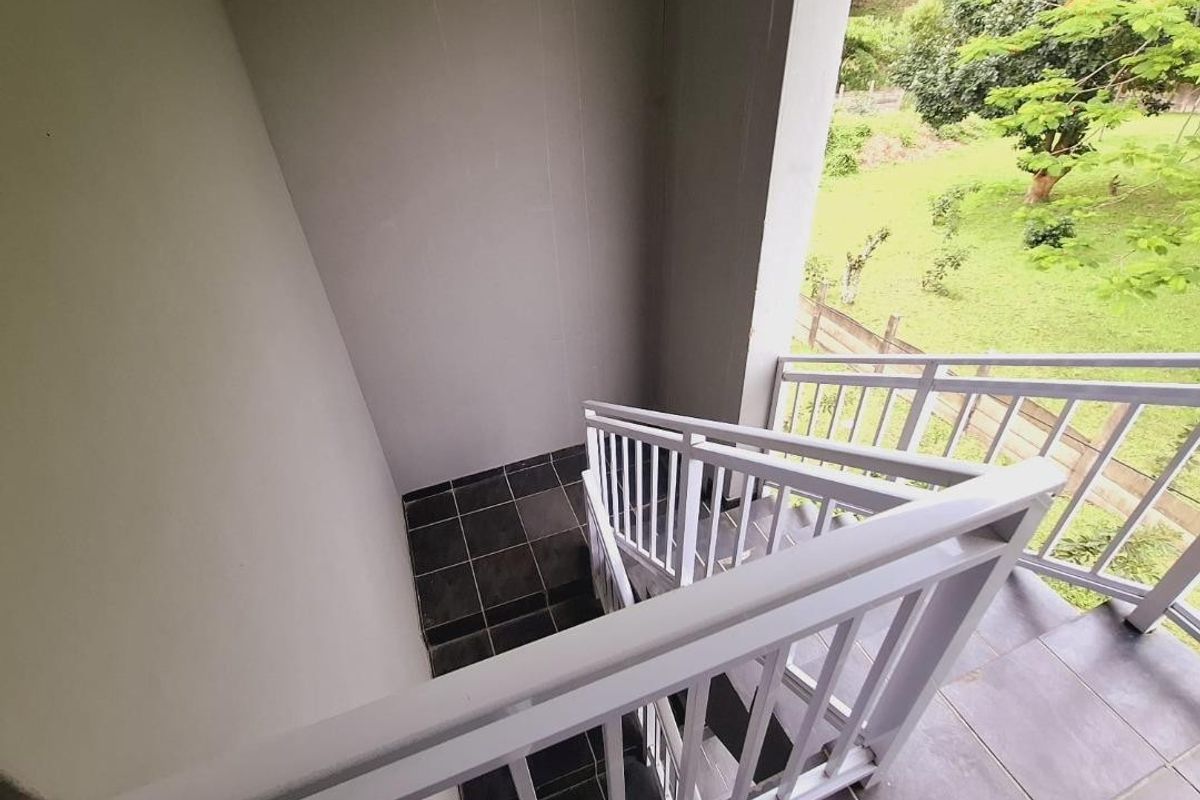 An outdoor staircase with a white metal balustrade and dark tiled steps, overlooking a green garden area.
