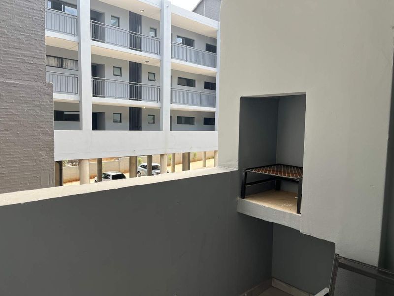 A private apartment balcony featuring a built-in braai area and metal safety railings, overlooking the complex courtyard.