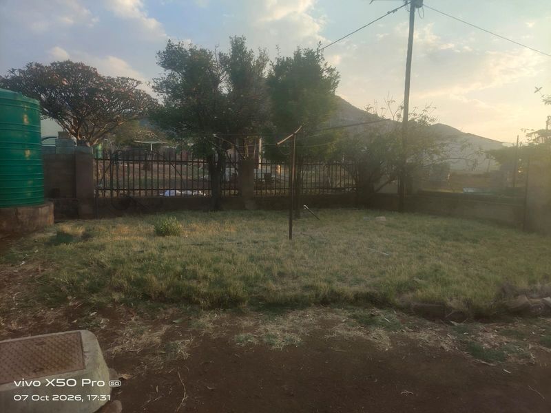 A backyard garden area featuring a water tank, metal perimeter fencing, and a rotary clothesline set against a mountain backdrop.