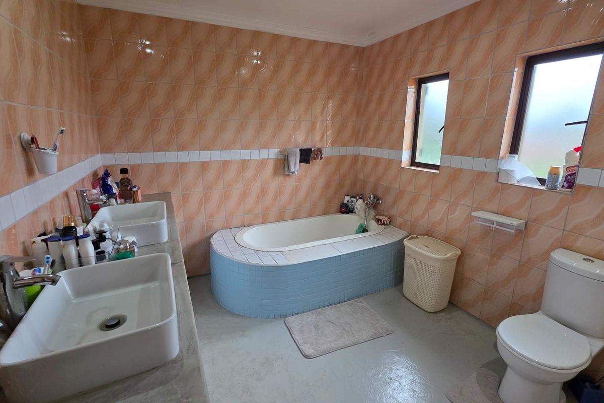 A dated bathroom featuring a double vanity, a built-in bathtub, and a toilet, finished with peach-toned wall tiles.